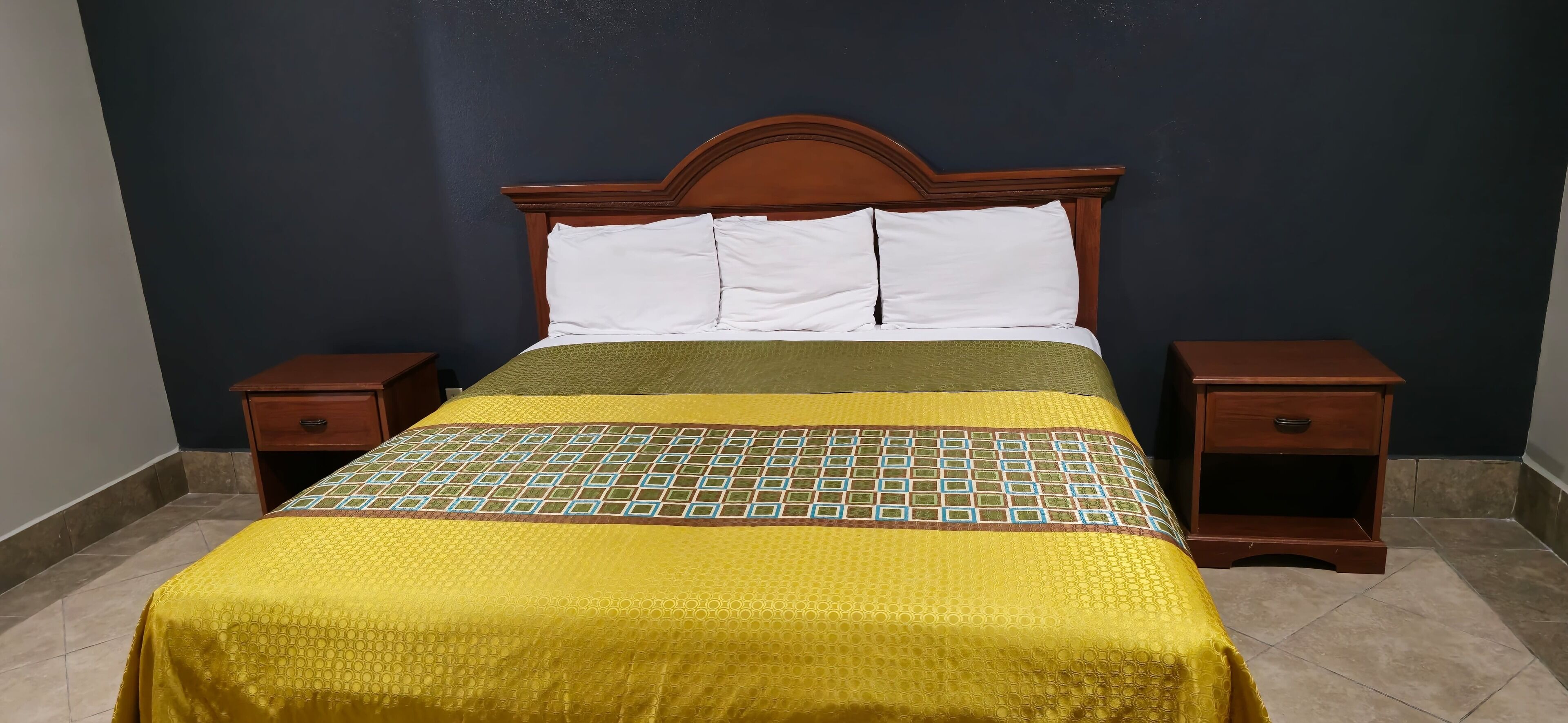 A bed with a wooden headboard, two nightstands, and a green and yellow patterned bedspread.