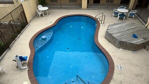 A swimming pool with a brick border, a diving board, and a wooden deck area with chairs and tables. - Texas Inn and Suites RGV (Edinburg)