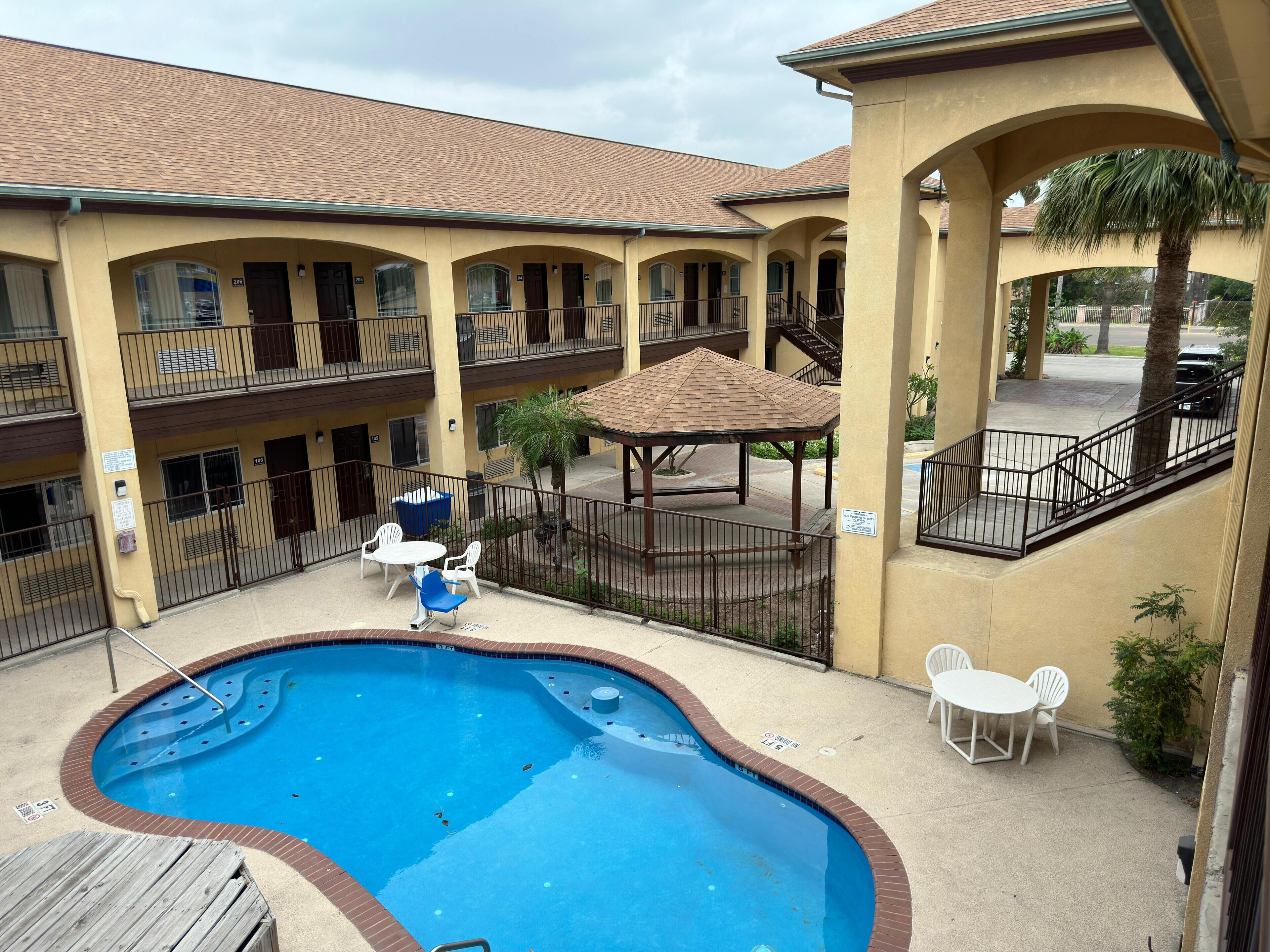A hotel with a swimming pool, outdoor seating, and a covered patio area.
