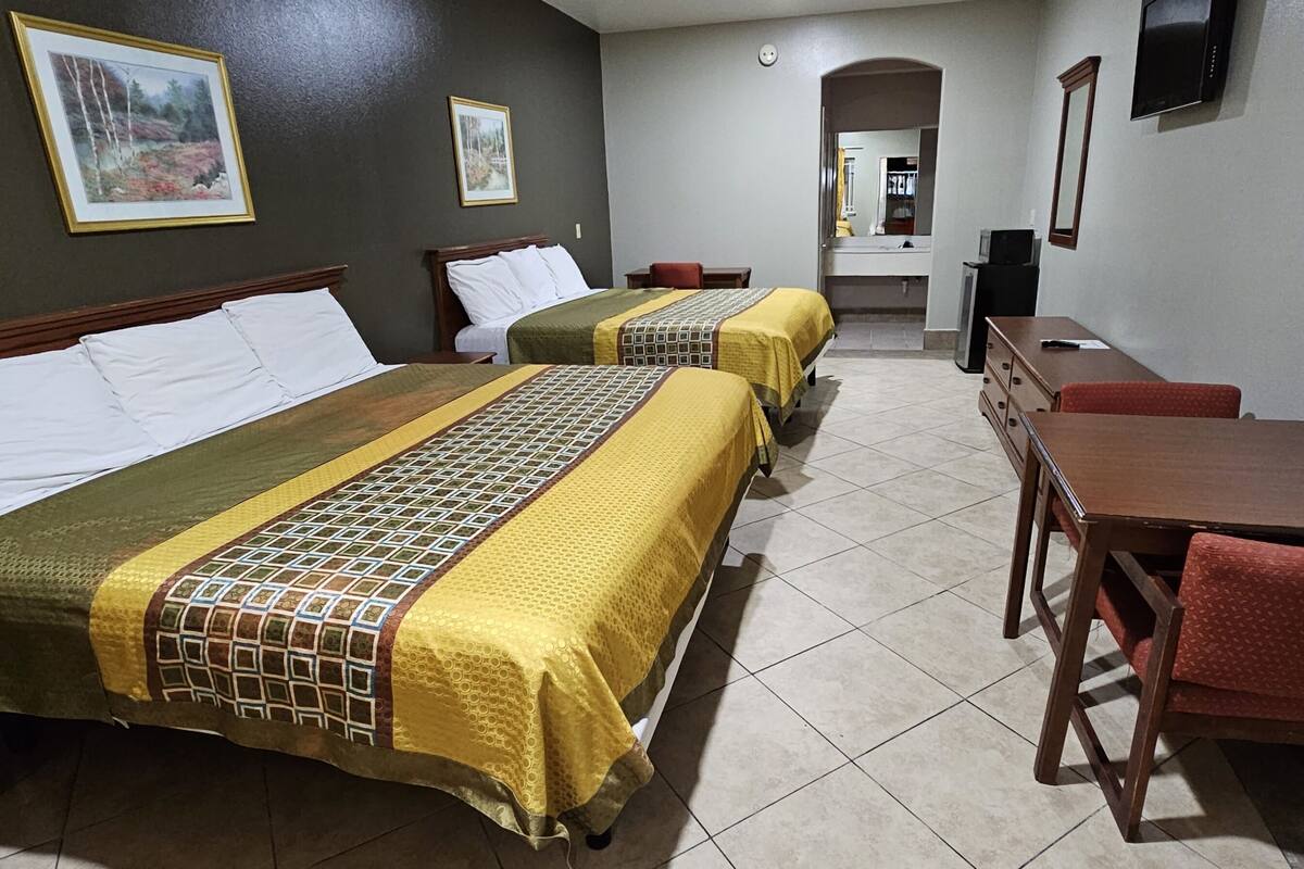 A hotel room with two beds, a desk, a chair, and a TV.
