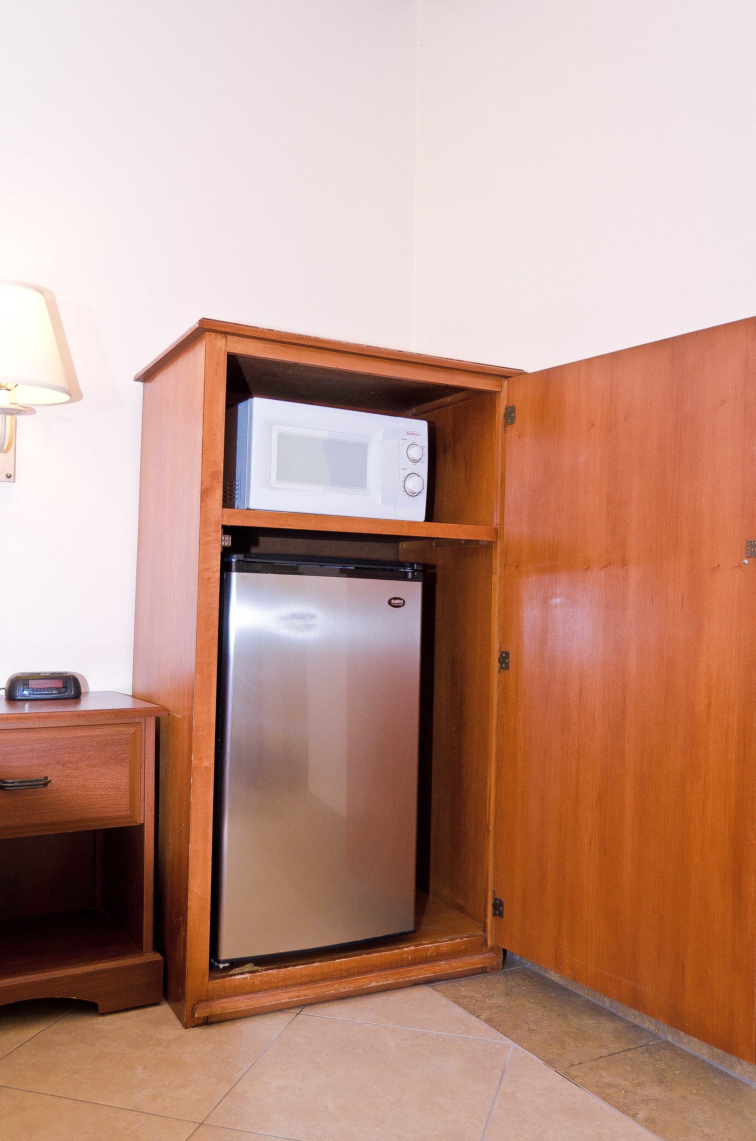 A compact kitchenette with a built-in microwave and refrigerator, wooden cabinetry, and a small countertop.