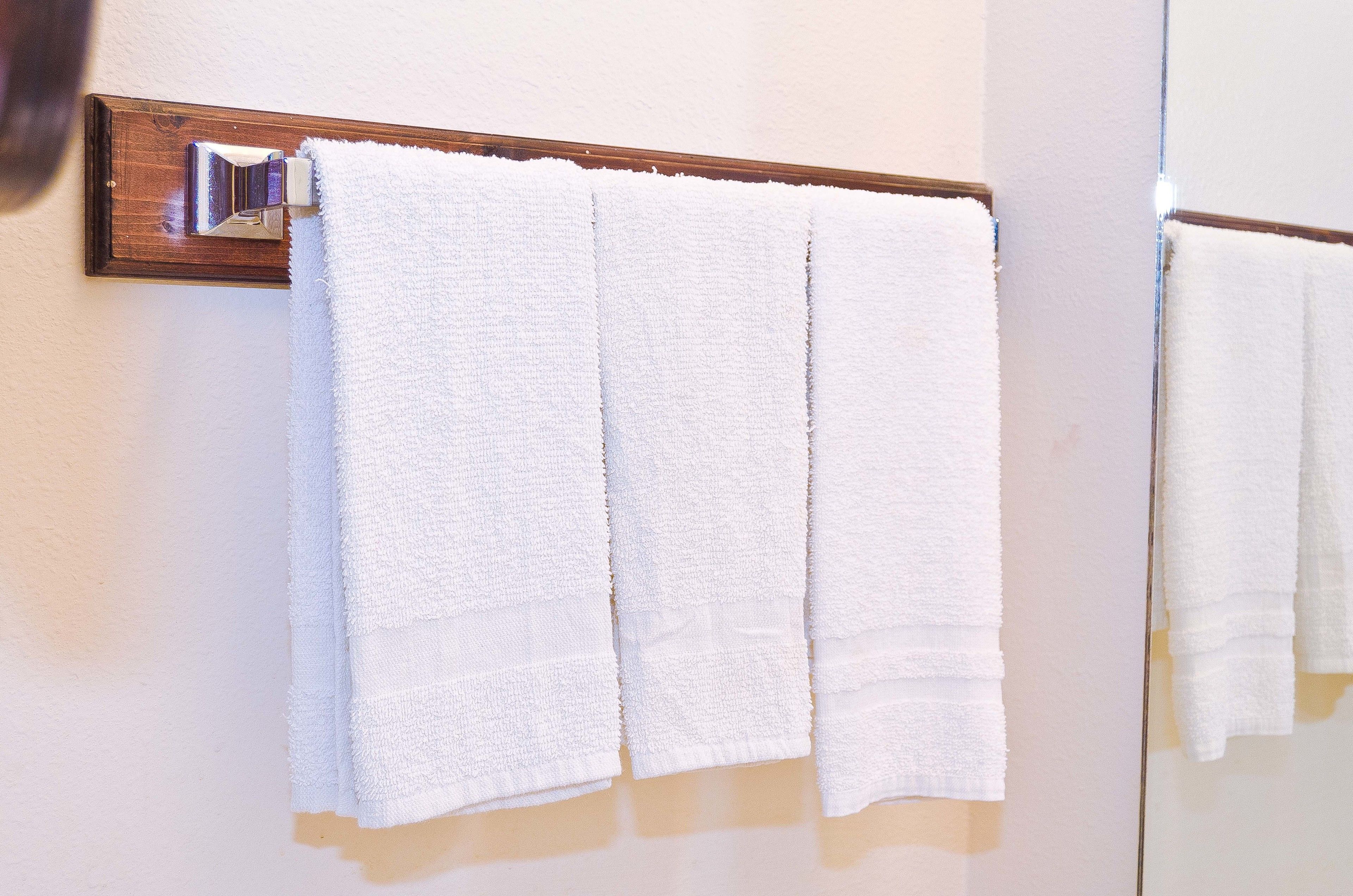 A white towel hanging on a wooden towel rack in a bathroom.