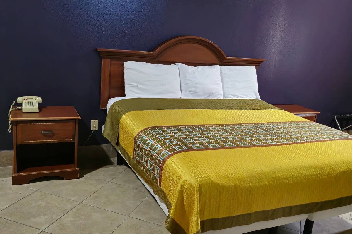A hotel room with a wooden bed, a nightstand with a telephone, and a heater.