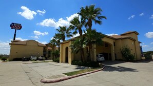 A Texas Inn hotel with a parking lot, palm trees, and a clear blue sky. - Texas Inn and Suites RGV (Edinburg)