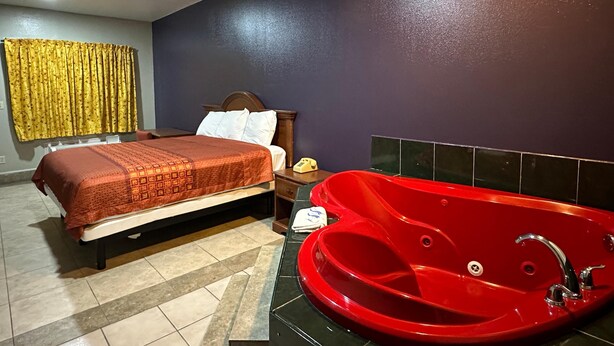A hotel room with a bed, a red bathtub, a ceiling fan, and a telephone on a nightstand. - Texas Inn and Suites RGV (Edinburg)