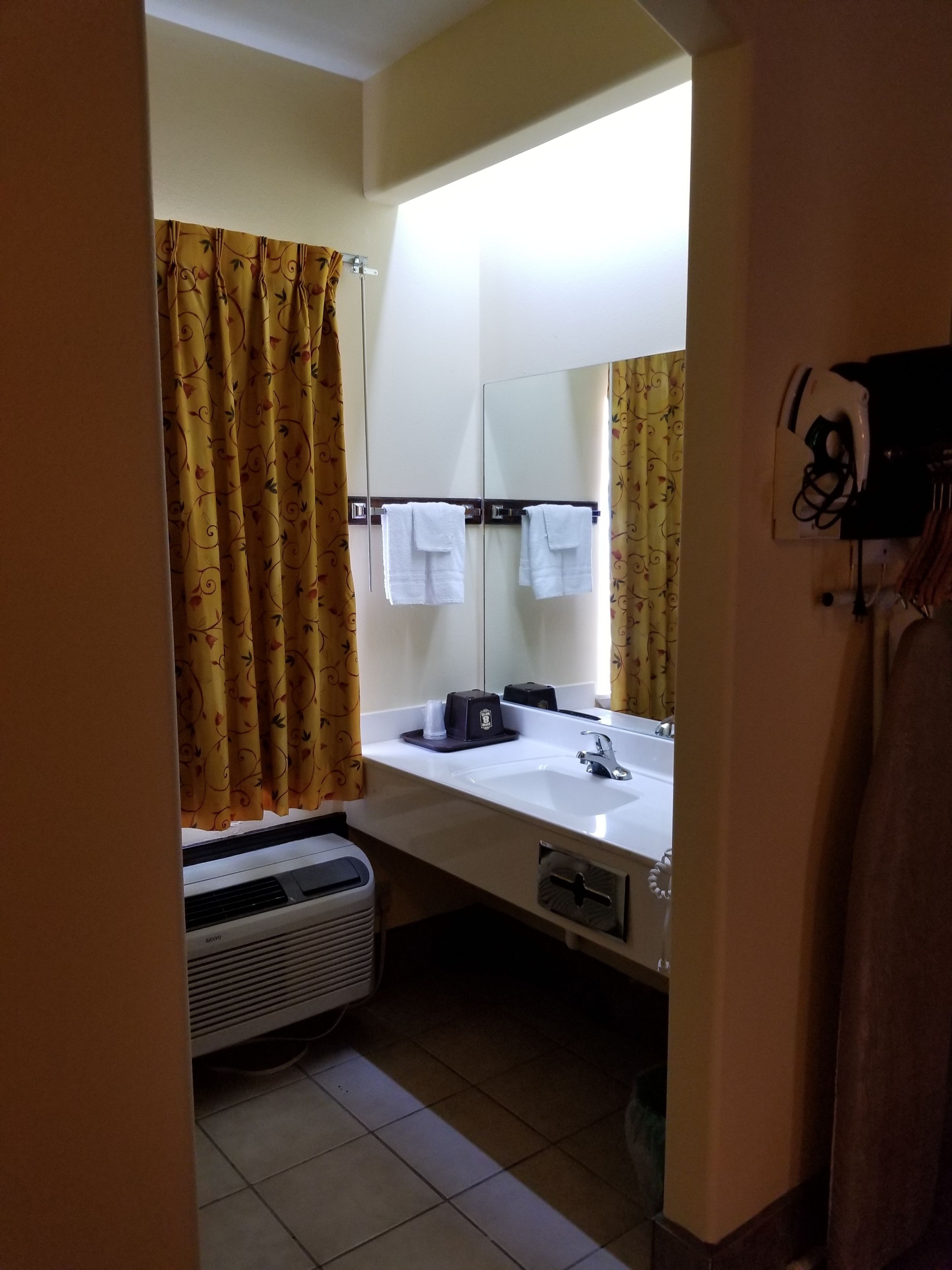 Un baño con lavamanos blanco, espejo, toallero y calentador.