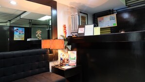 A reception area with a black sofa, a desk with a lamp, and a bulletin board with notices. - Asian Mansion Il (Makati)
