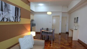A living room with a sofa, a dining table with chairs, and a kitchen area in the background. - Asian Mansion Il (Makati)