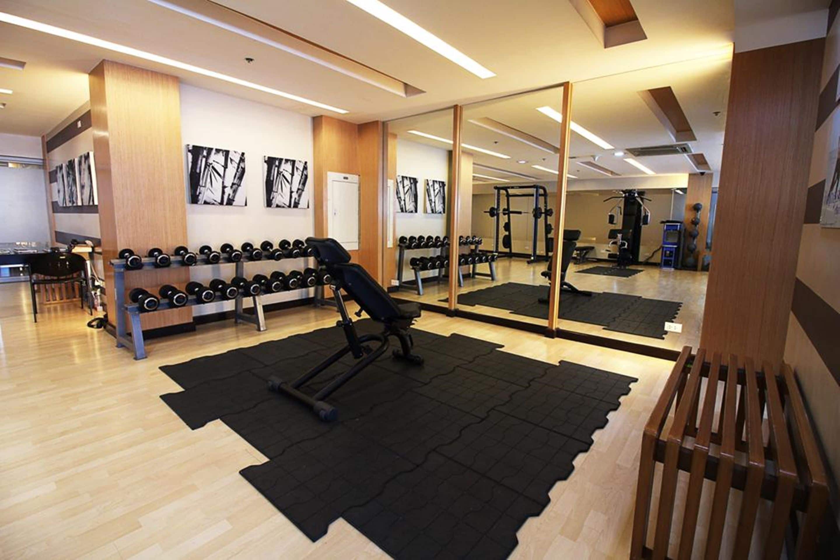 A gym with exercise equipment, a mirrored wall, and a wooden floor.