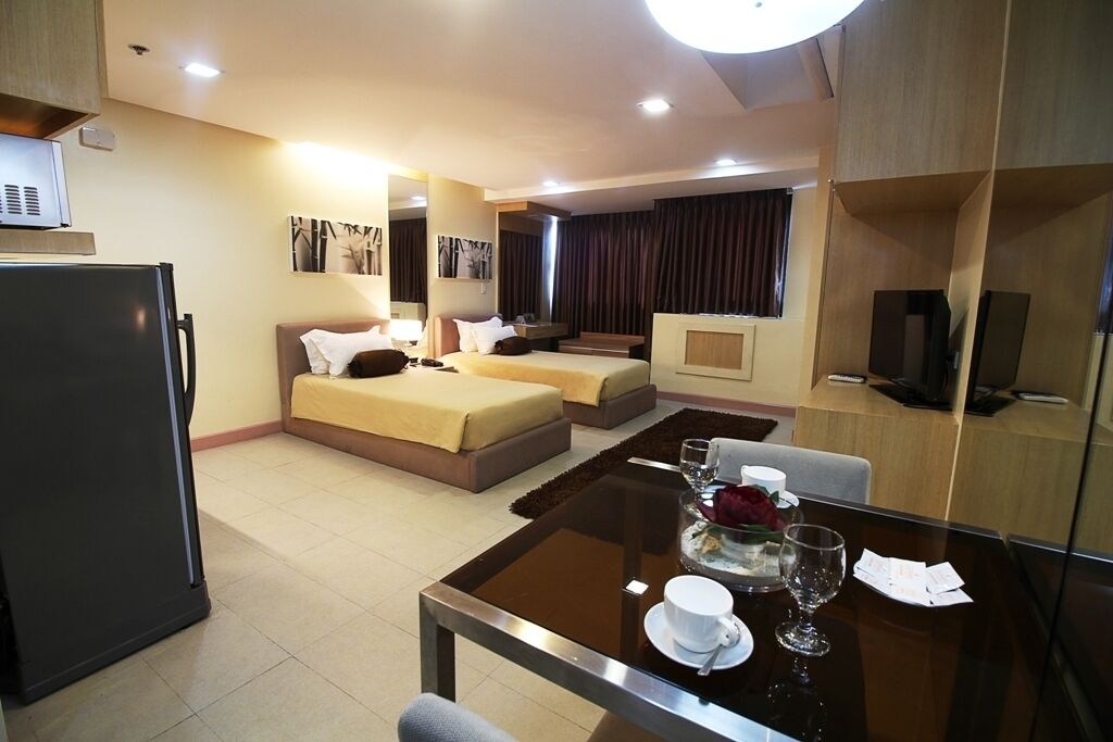A hotel room with a bed, a sofa, a dining table with a glass top, and a television.