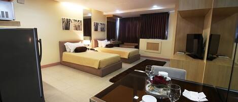 A hotel room with a bed, a sofa, a dining table with a glass top, and a television.