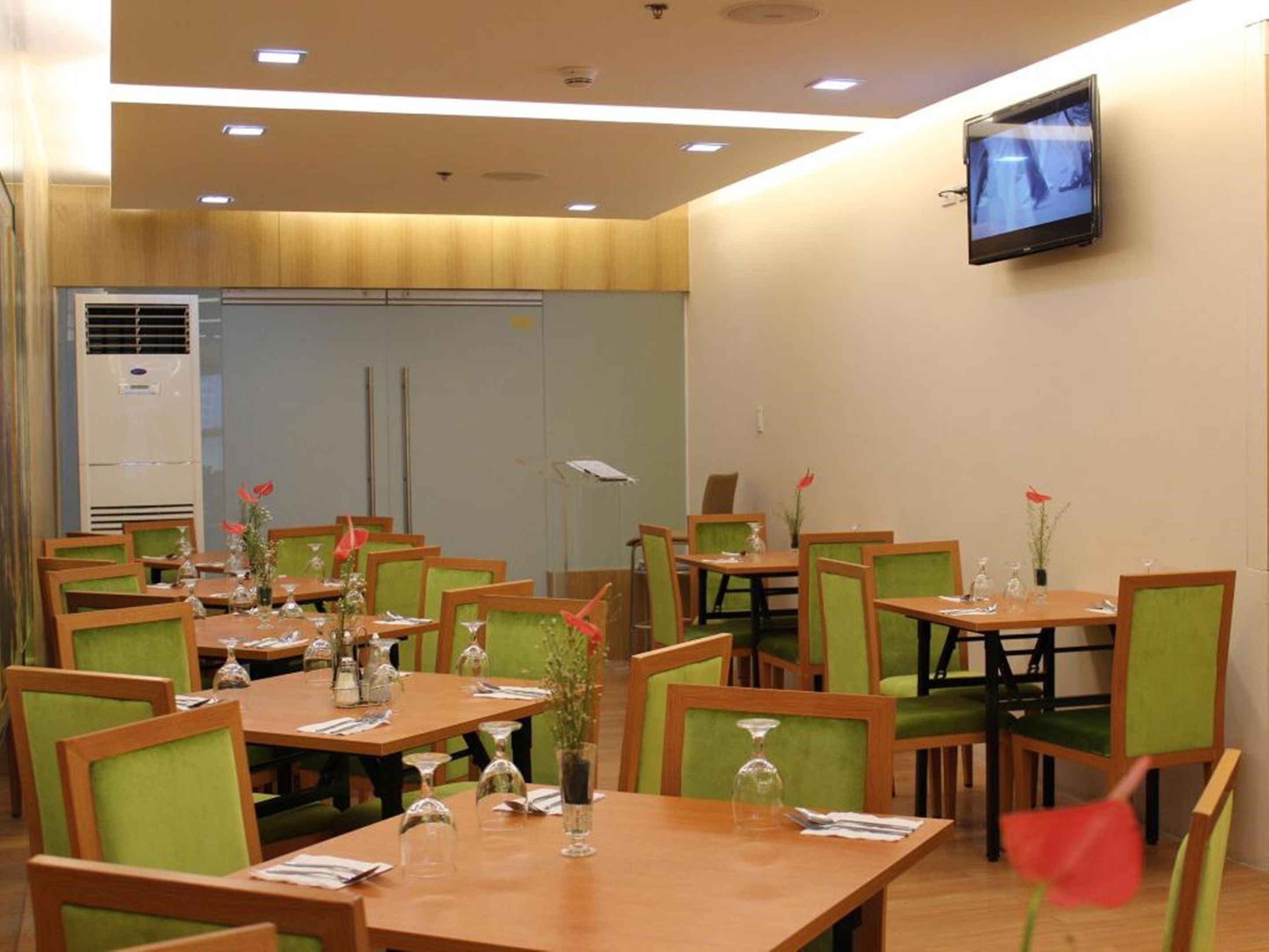 En restaurang med flera bord och stolar, en tv-skärm som hänger på väggen och en luftkonditioneringsanläggning i bakgrunden.