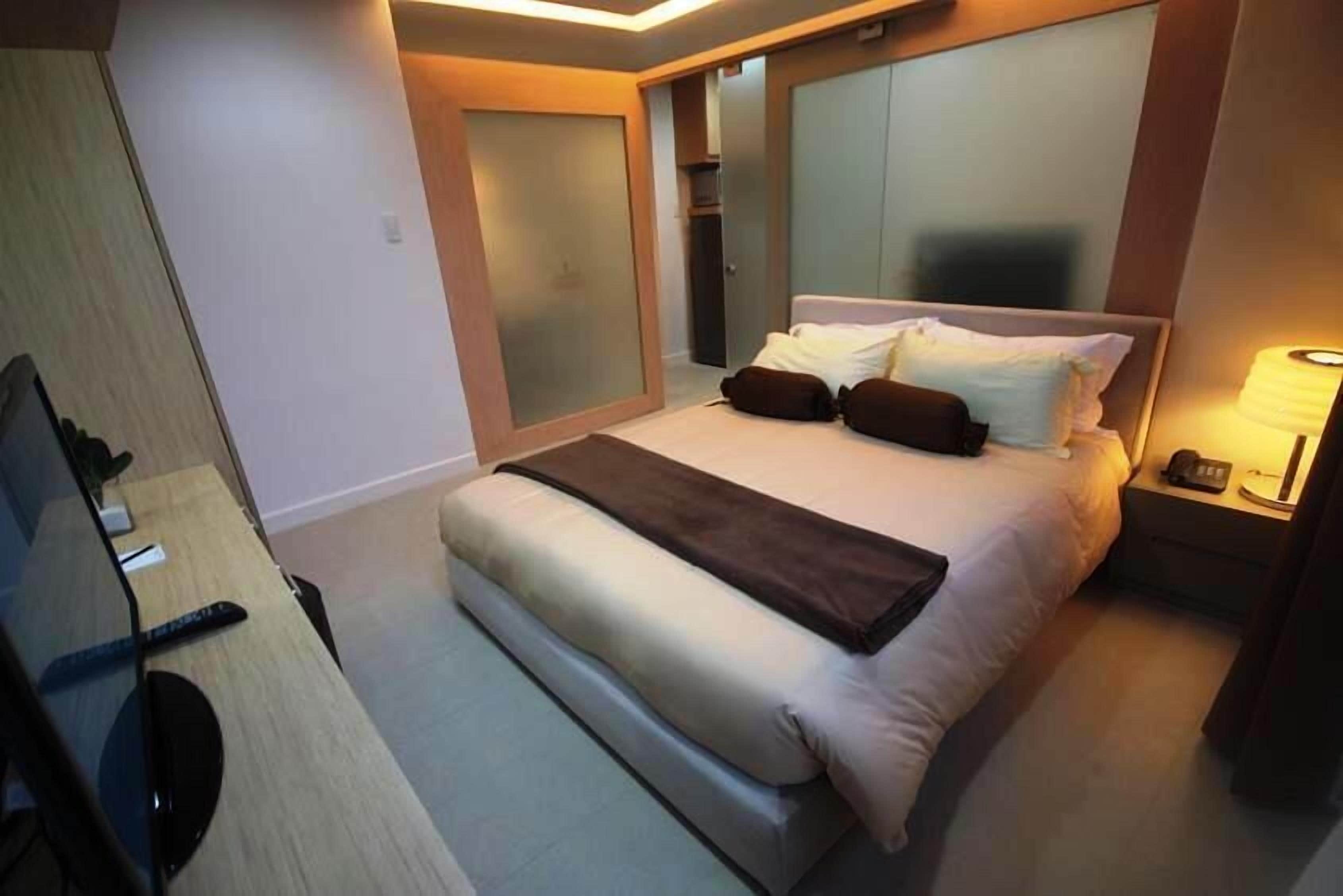 A hotel room with a bed, bedside table, lamp, and a TV.