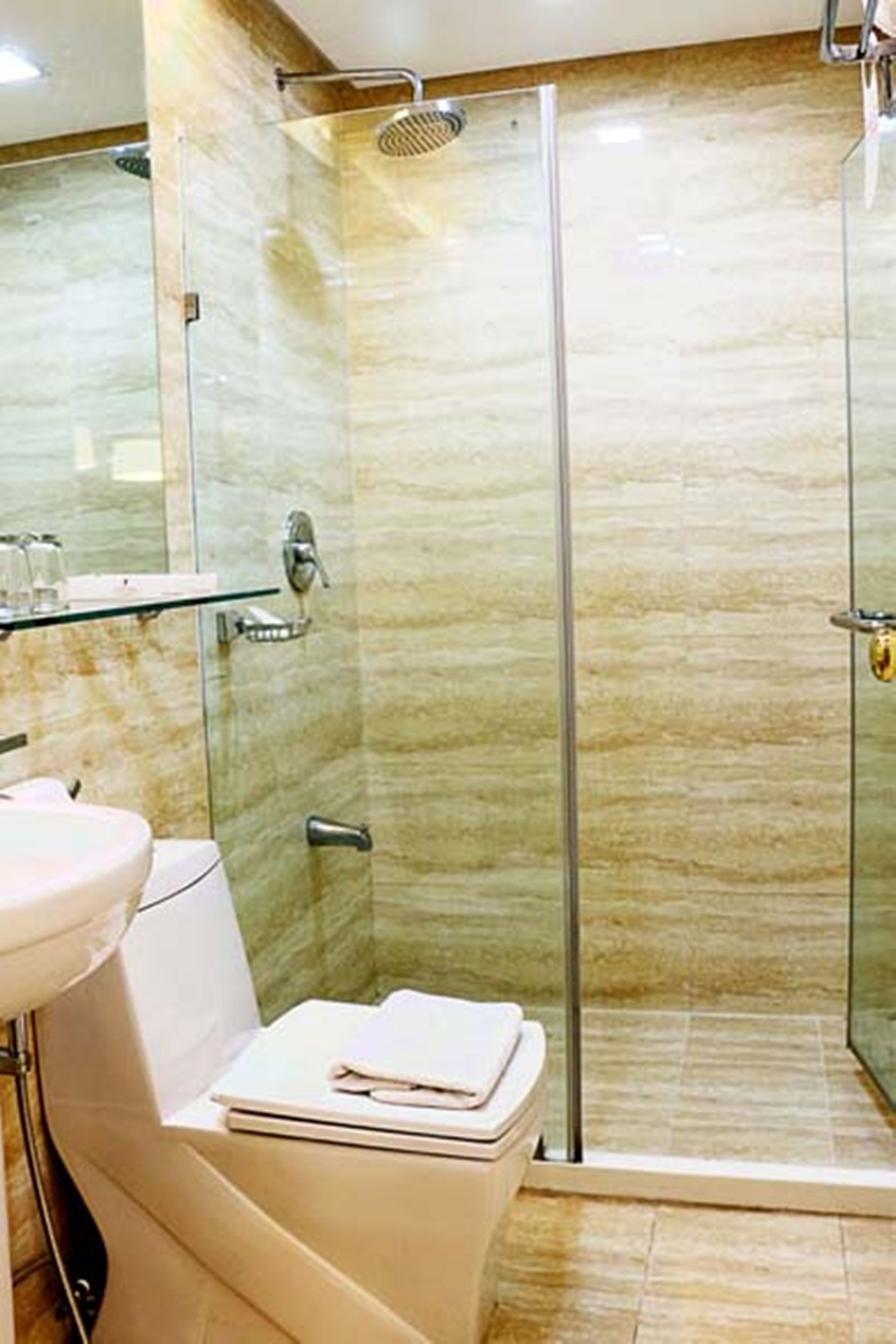 A modern bathroom with a glass-enclosed shower, a white sink, and a glass shelf with toiletries.