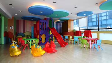 A brightly colored indoor play area with various play structures, tables, and chairs.