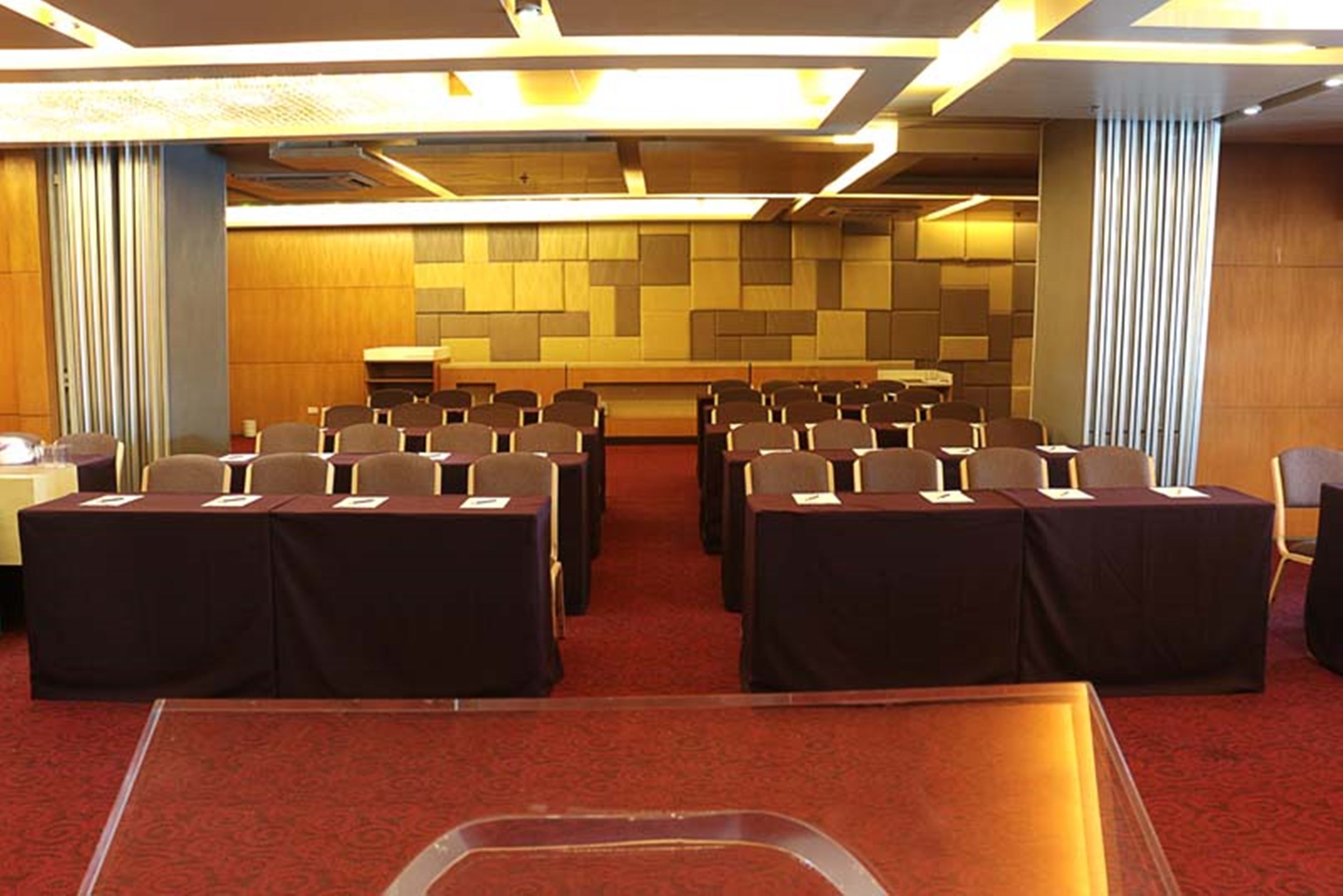 A conference room with rows of tables and chairs, a carpeted floor, and a wooden panel wall.