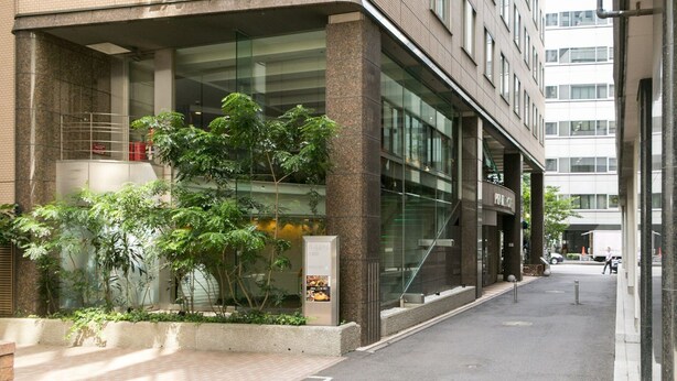 L’extérieur de l’hôtel Pearl présente un design moderne, avec de grandes fenêtres en verre et un espace extérieur bien entretenu agrémenté de plantes.