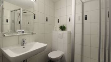 Un baño moderno con lavamanos, inodoro y zona de ducha blancos.