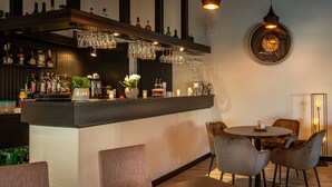 A bar area with a counter, shelves of bottles, and hanging glasses. There are chairs and a table with a candle and decorative items. - Hulsman (Valkenburg aan de Geul)