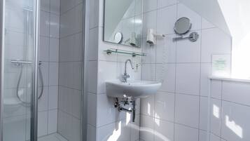 Un baño moderno con cabina de ducha de vidrio, un lavabo blanco con un espejo encima y un secador de pelo en la pared.