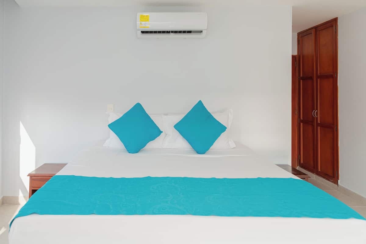 Un dormitorio con una cama, dos almohadas, una colcha azul, un armario de madera y un equipo de aire acondicionado.