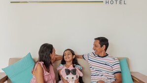Uma família sentada em um sofá com o logotipo do 'Sanha Plus Hotel' ao fundo.