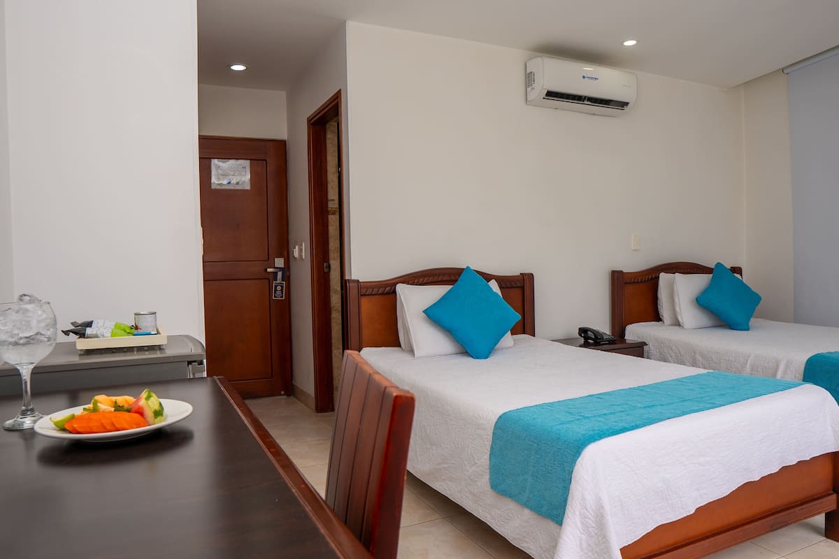 Habitación de hotel con dos camas, un escritorio y una bandeja de fruta, además de un aire acondicionado.