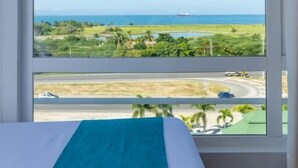 Quarto com uma grande janela que oferece vista para a paisagem costeira, incluindo uma estrada e vegetação.
