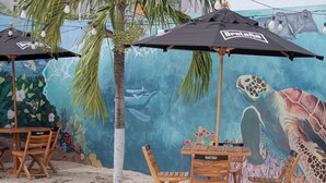 Mobiliário de exterior com cadeiras e mesas de madeira, guarda-sóis e um mural com vida marinha.