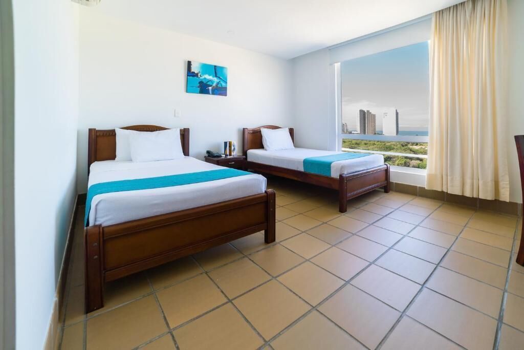 A hotel room with two beds, a large window with a city view, and a painting on the wall.
