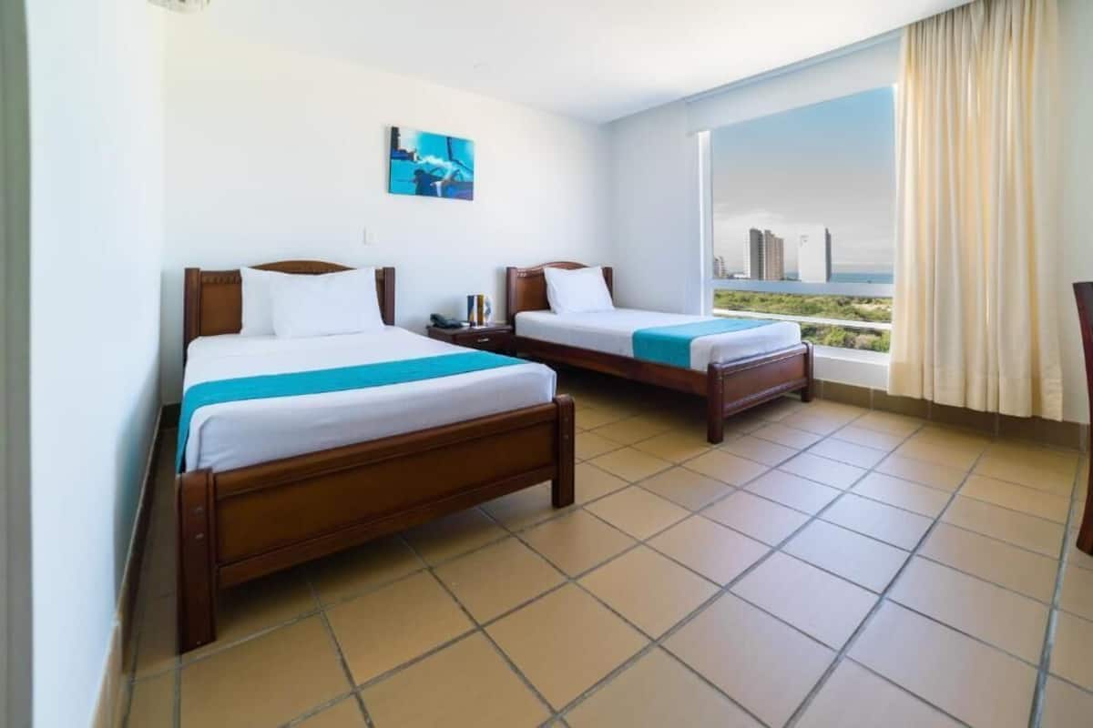 Una habitación de hotel con dos camas, un ventanal con vista a la ciudad y un cuadro en la pared.