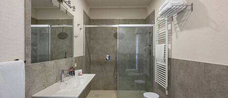 A bathroom with a glass-enclosed shower, a sink, a bidet, and a towel rack.