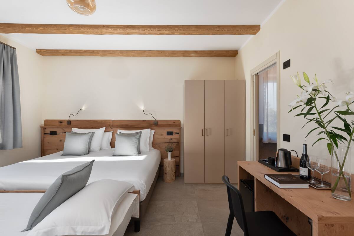 A bedroom with a wooden headboard, two beds, a desk with a chair, a wardrobe, and a bedside table with a lamp.
