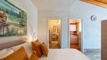 Quarto com cama, almofadas, um quadro, um corredor e uma área de cozinha.