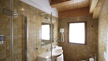 Een badkamer met een douchecabine van glas, een wastafel, een toilet en een raam.