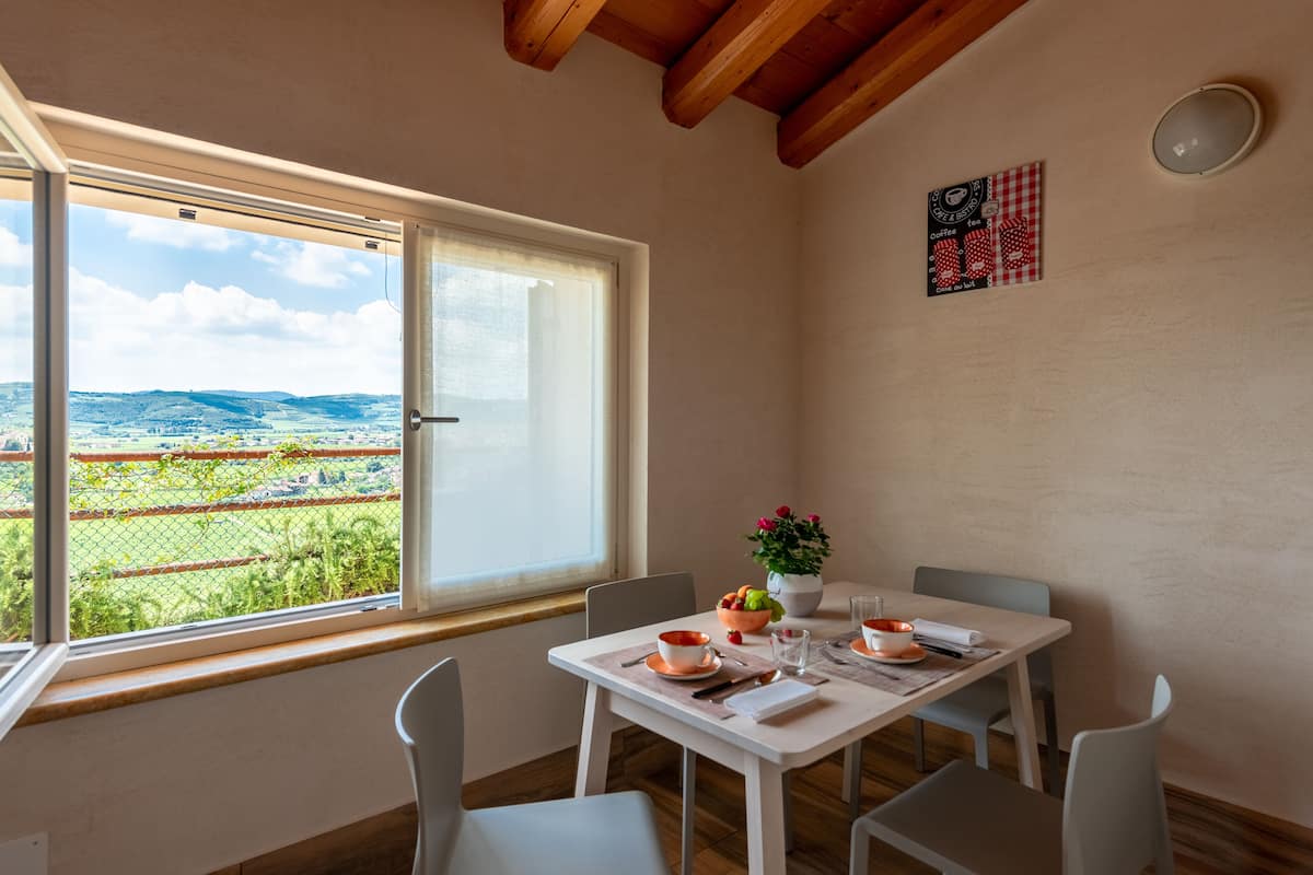 A dining area with a table set for two, a window with a view of a green landscape, and a wall-mounted sign.