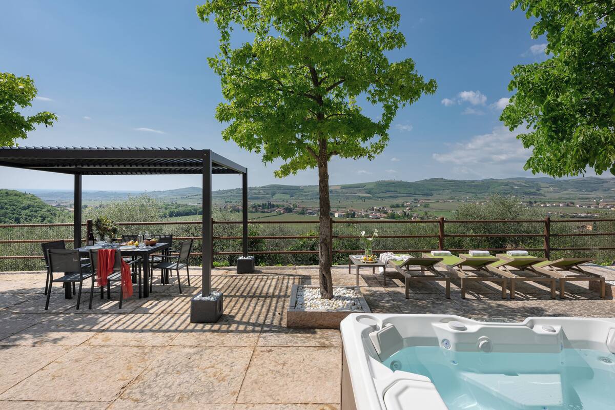 A terrace with a table and chairs, a hot tub, and a view of the countryside.