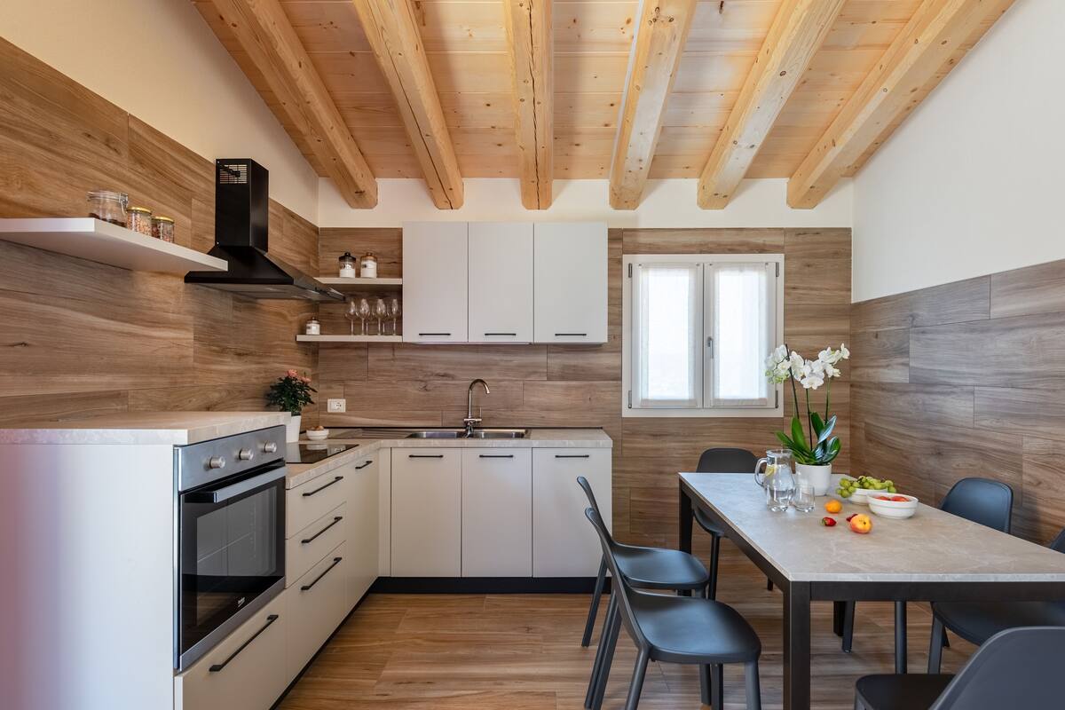 A modern kitchen with wooden beams, white cabinets, and a dining area with a table and chairs.