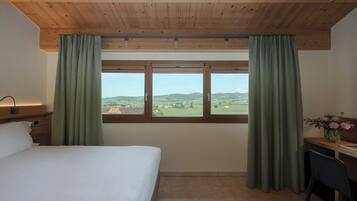 Une chambre à coucher comprenant un lit, un bureau, une chaise, une fenêtre avec des rideaux et une vue sur la campagne.
