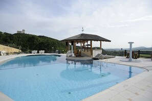 Une piscine agrémentée d’un belvédère, de chaises longues et d’un mur en pierre.