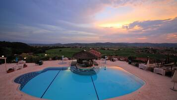A swimming pool with a gazebo, lounge chairs, and a view of the countryside.