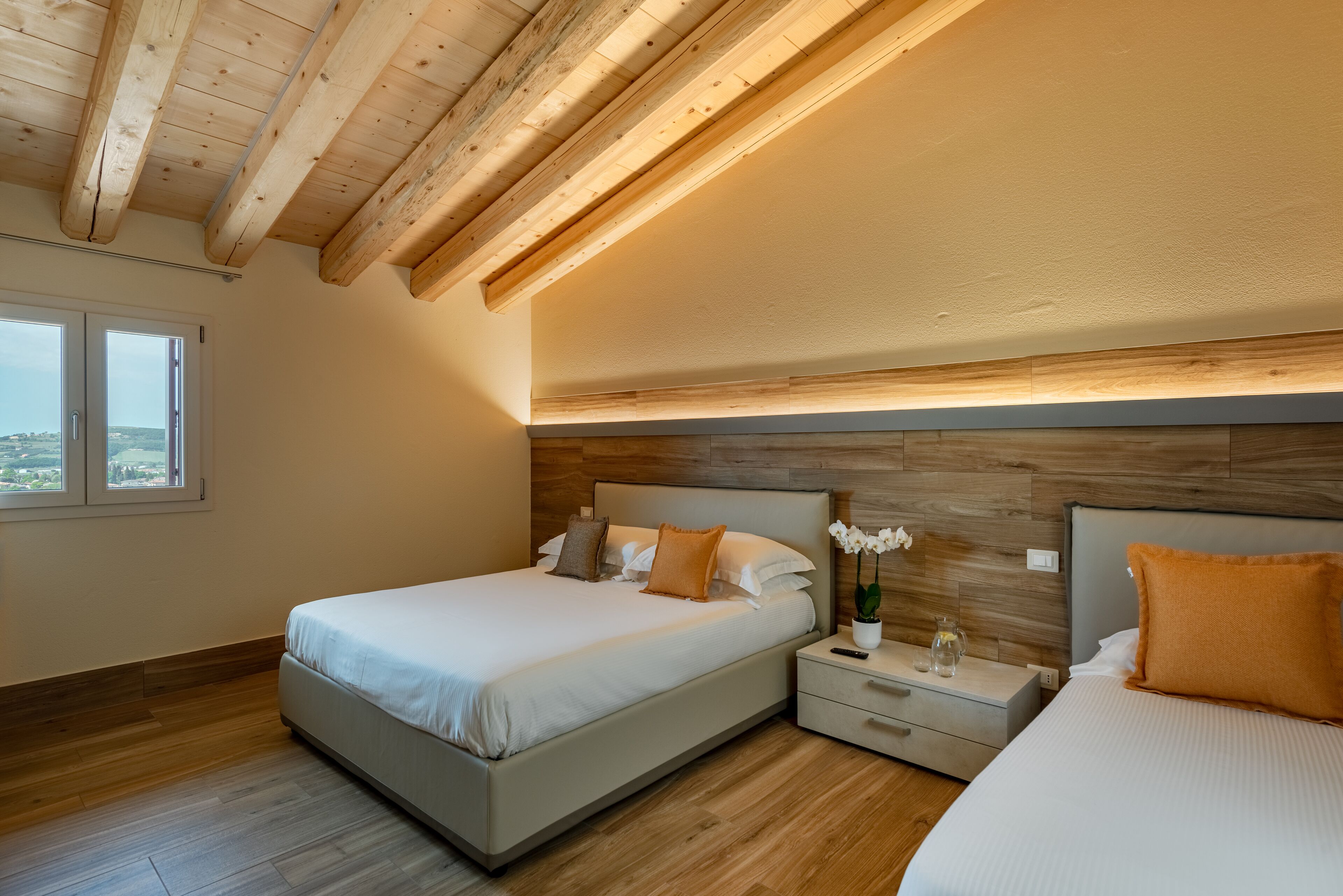A bedroom with a wooden ceiling, a large bed, a nightstand, and a window.