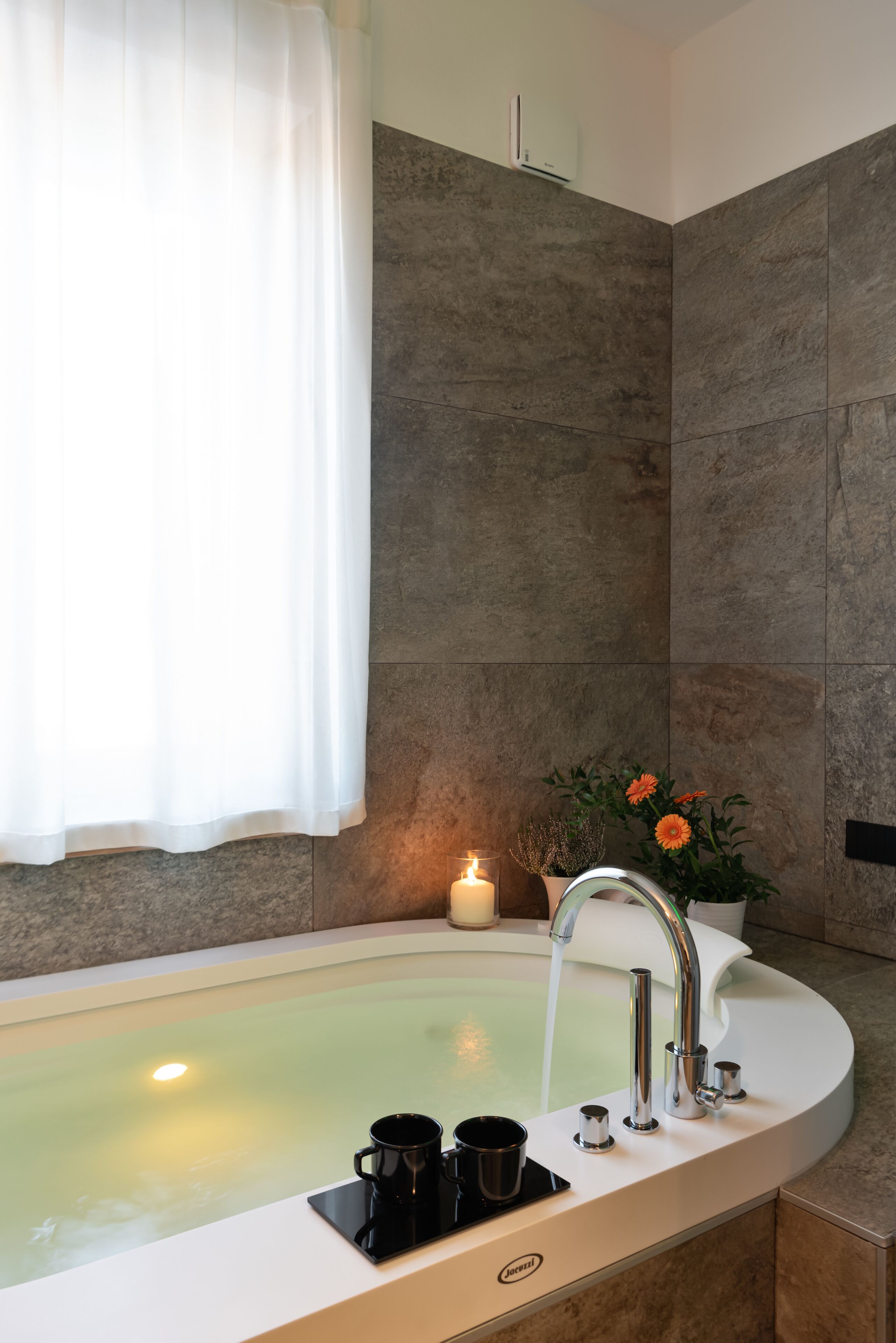 Une salle de bain moderne avec une baignoire sur pieds, un lavabo blanc et une plante en pot aux fleurs orange.