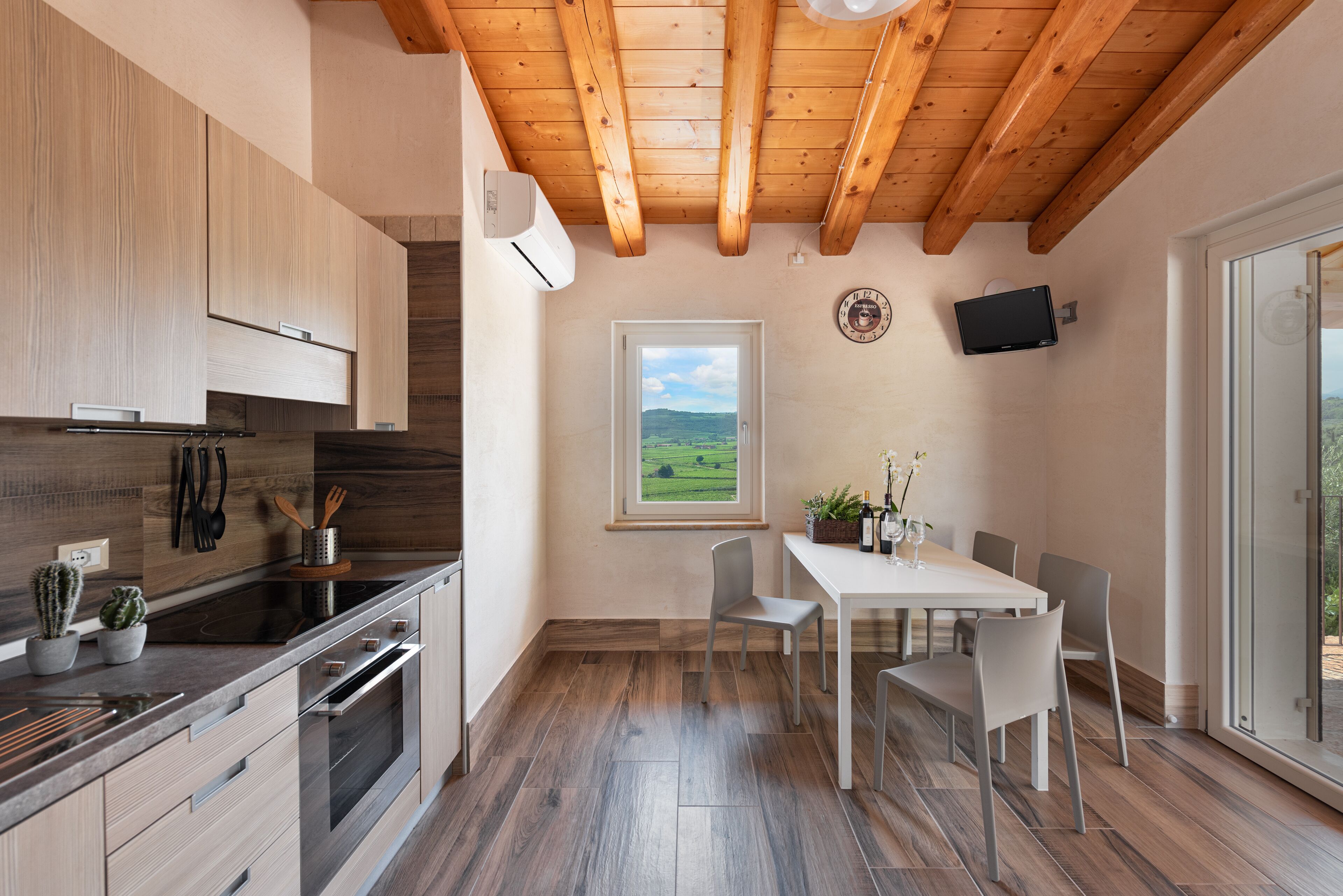 A modern kitchen with wooden beams, a dining area with a table and chairs, and a window with a view of the countryside.
