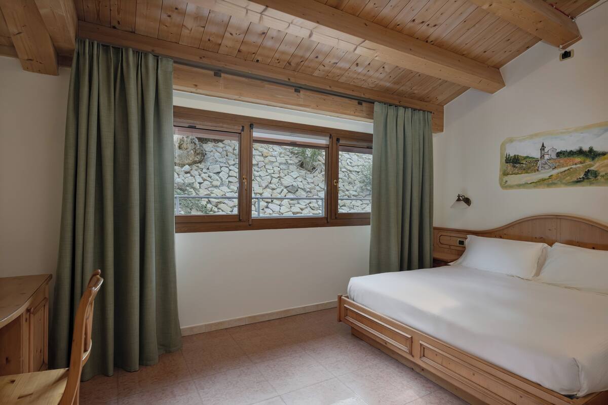 A bedroom with a wooden ceiling, a bed, a desk, and a window with curtains.