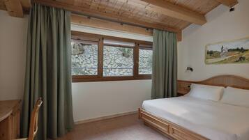 Un dormitorio con techo de madera, una cama, un escritorio y una ventana con cortinas.