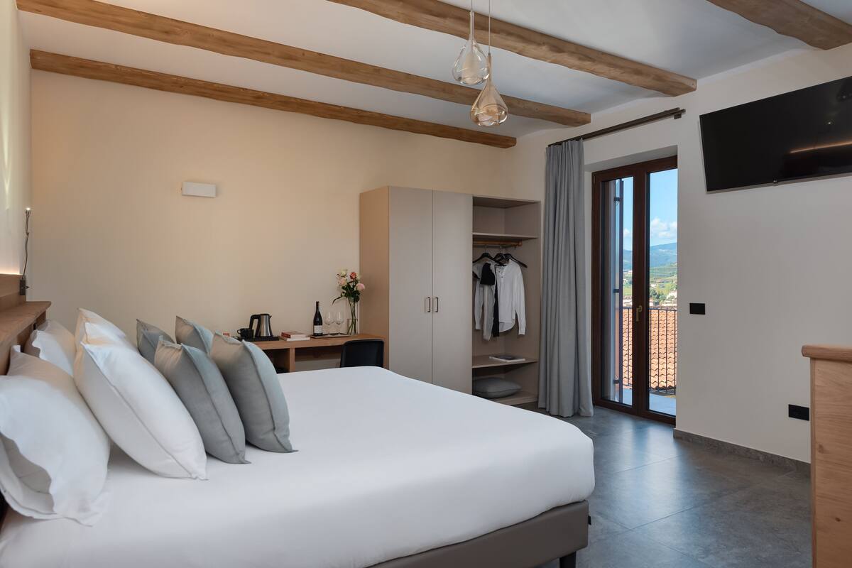 A bedroom with a large bed, a desk with a chair, a wardrobe, and a TV mounted on the wall.