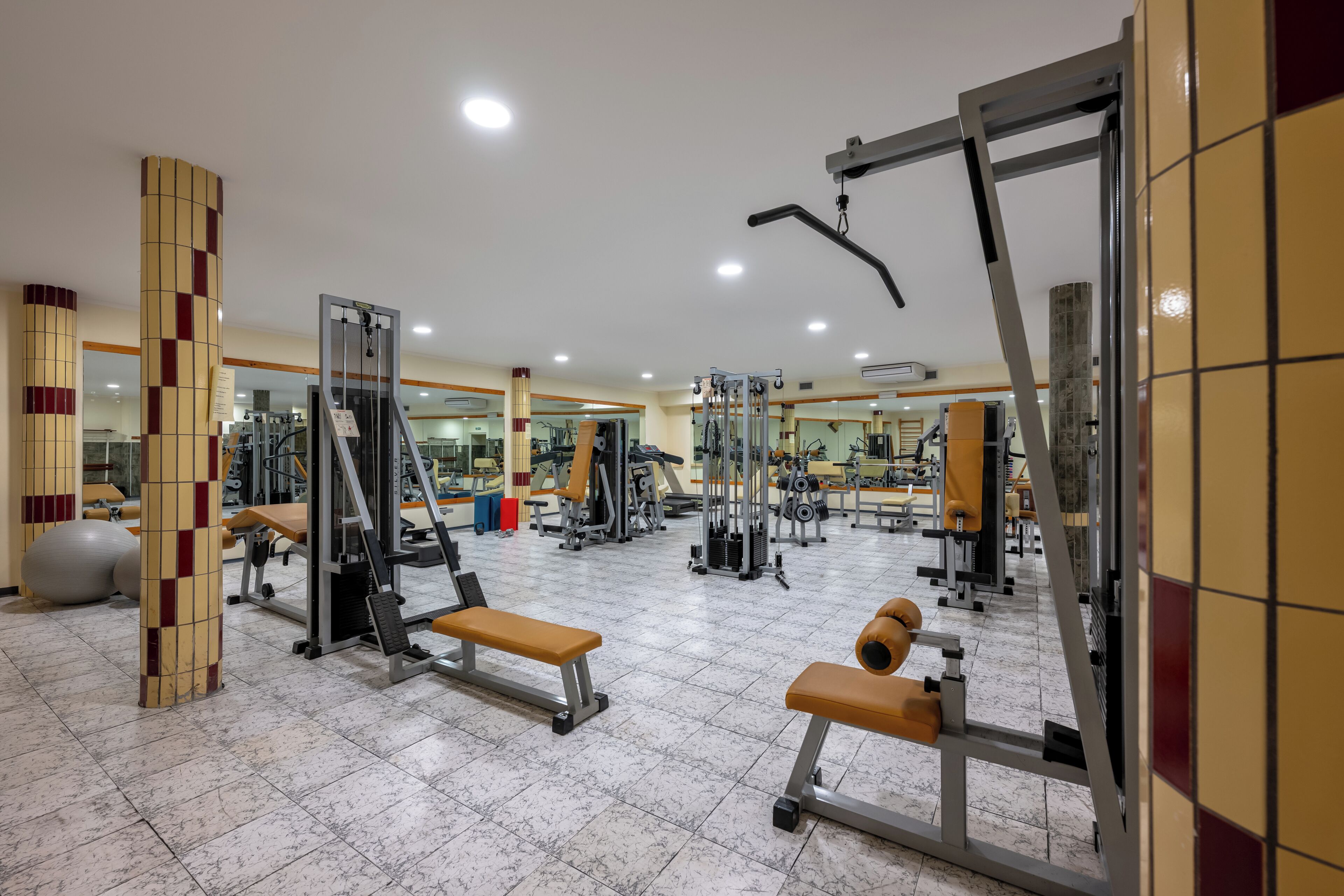 A gym with various exercise equipment, benches, and a mirrored wall.