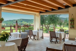 Une terrasse extérieure avec des tables et des chaises, une vue sur la campagne et un plafond en bois.
