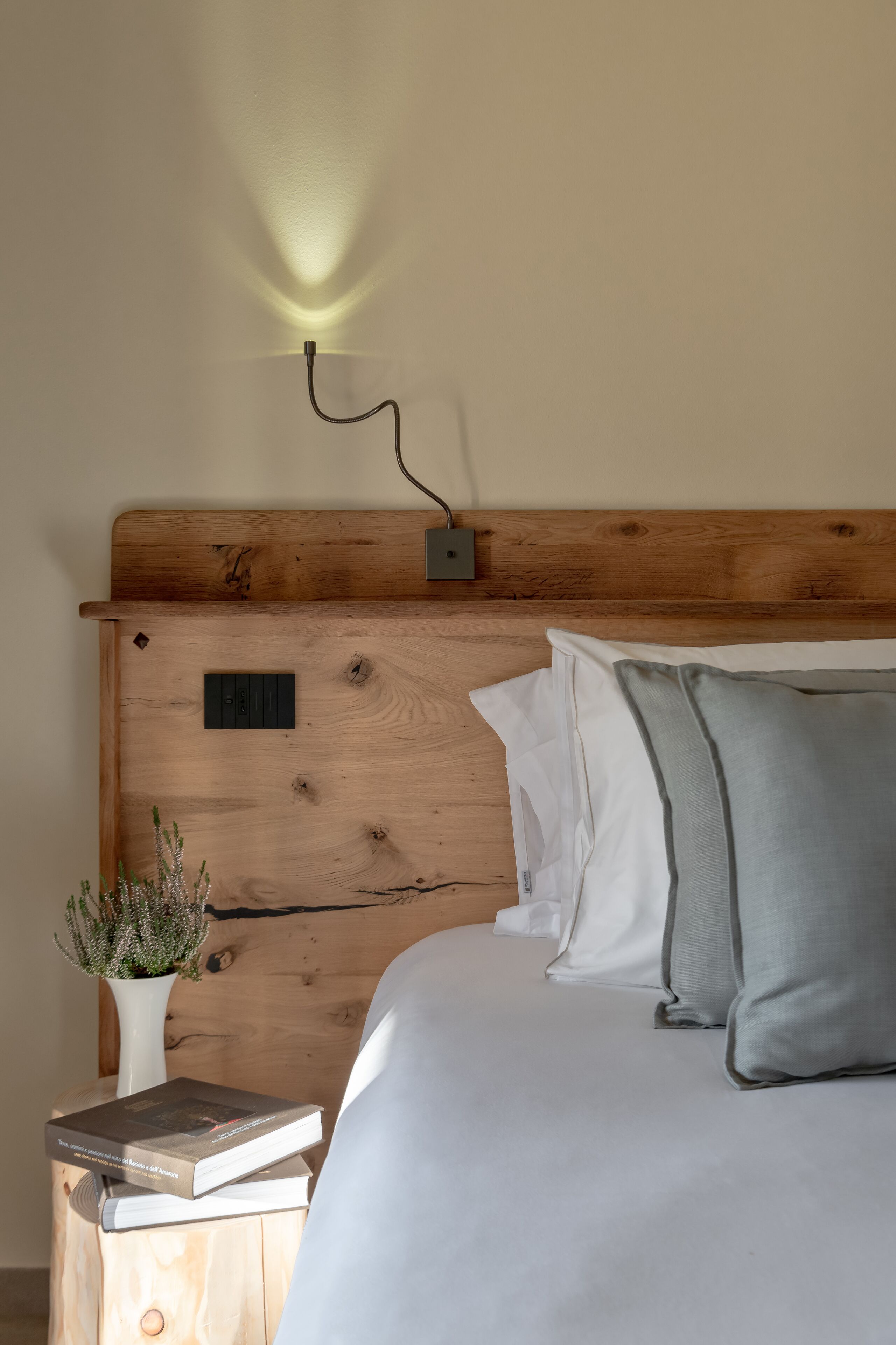 Un letto rifatto con cuscini, un comodino con un libro e un vaso, e un lampadario fissato al muro.